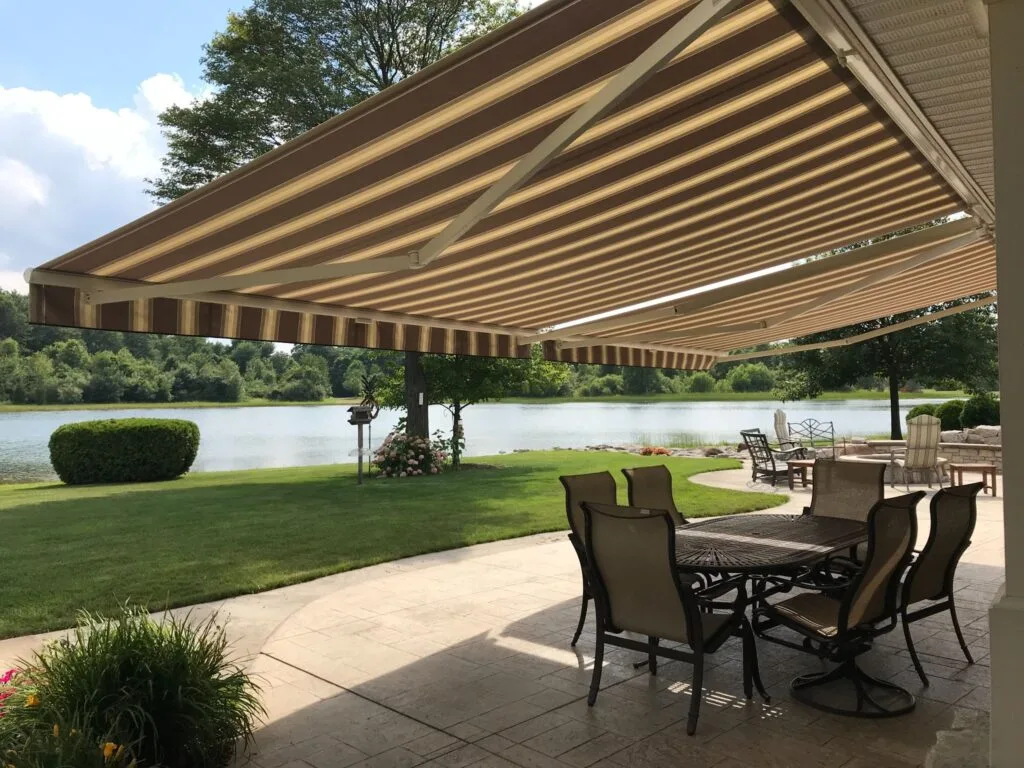 A brown striped Sunesta awning shading a patio beside a lake