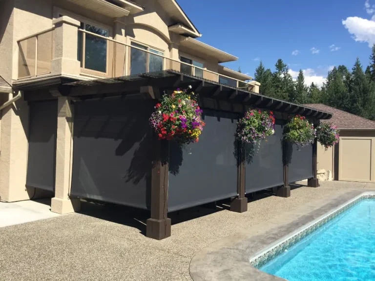 Dark retractable screens lowered on a poolside pergola with hanging flowers