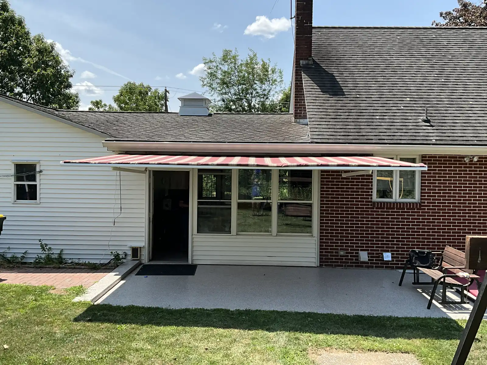 A striped retractable awning over the patio of a brick home