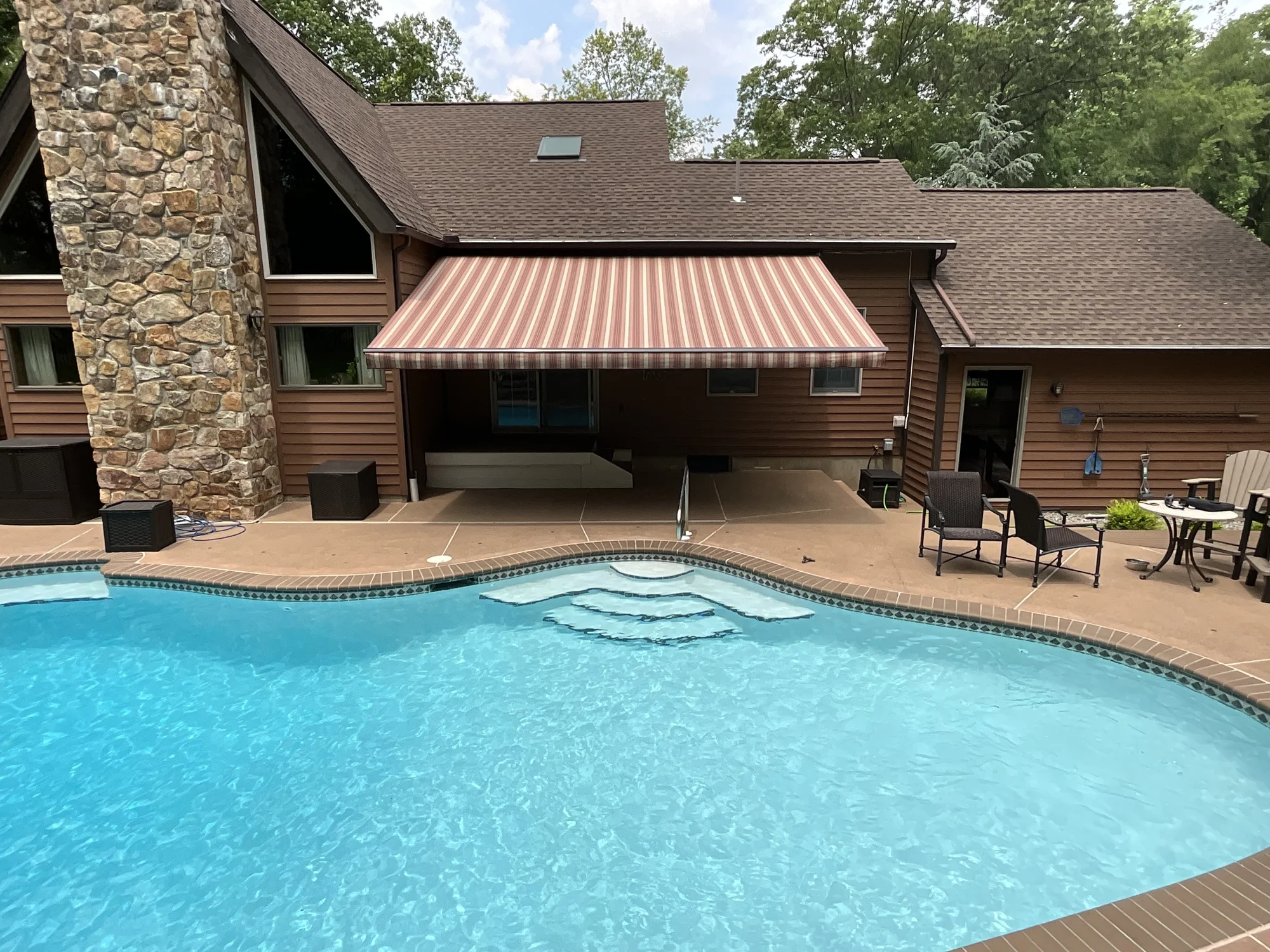 A striped retractable awning shading the patio beside a backyard pool